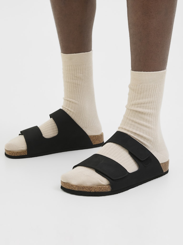 Black sandals with cork sole worn with white socks on a white background