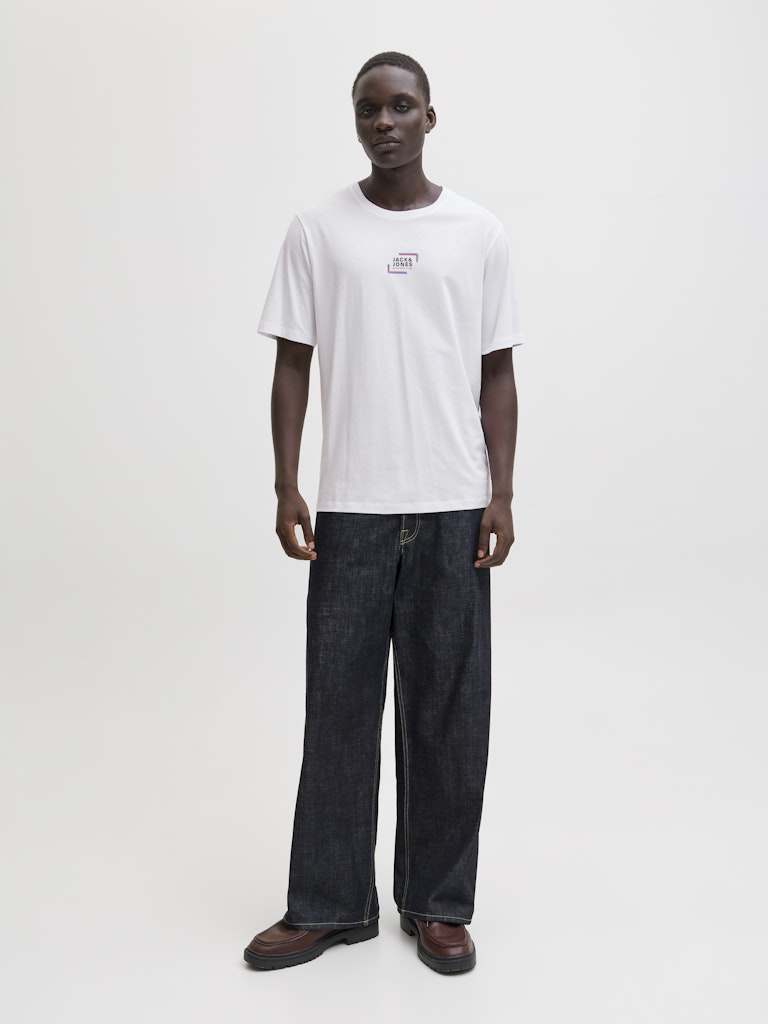 Person wearing a white t-shirt and dark jeans on a plain background