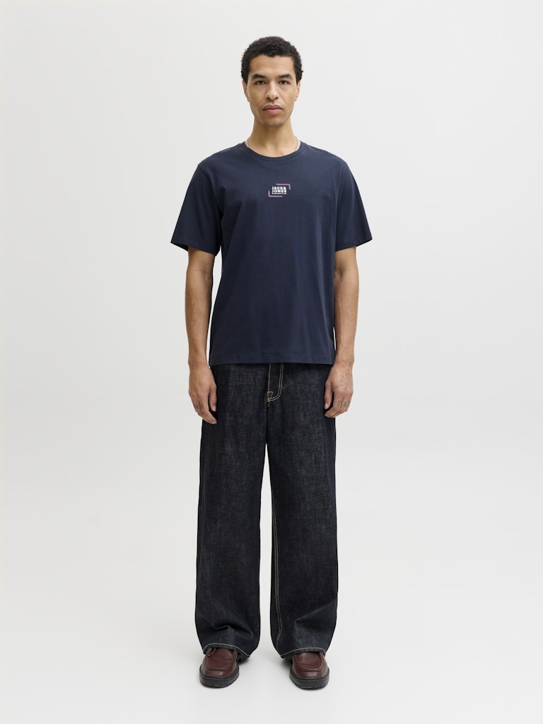 Man wearing a navy short sleeve tee with a jack & Jones logo on the chest with a pair of dark navy jeans