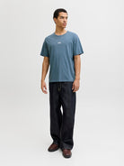 Man wearing a blue short sleeve tee with a jack & Jones logo on the chest with dark navy jeans