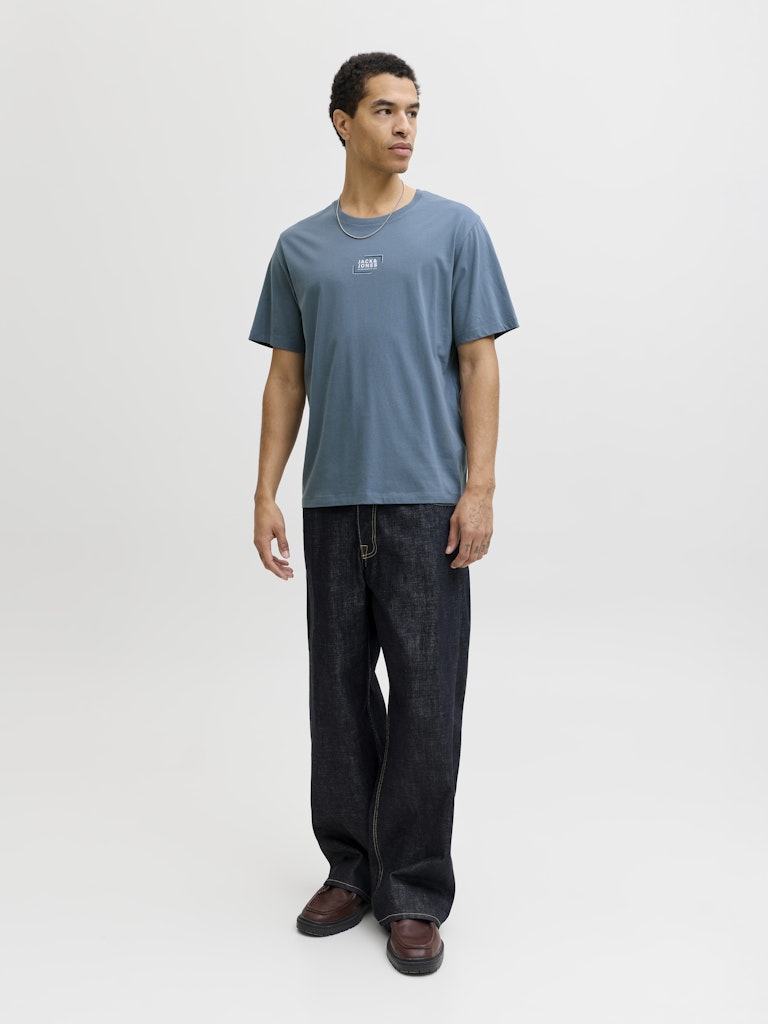 Man wearing a blue short sleeve tee with a jack & Jones logo on the chest with dark navy jeans