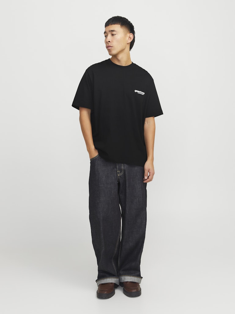 Person wearing a black t-shirt with a logo and dark jeans on a white background