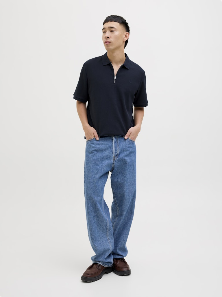 Person wearing a navy polo shirt and blue jeans on a white background