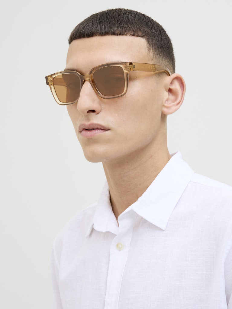 Man wearing gold sunglasses and a white shirt against a light background