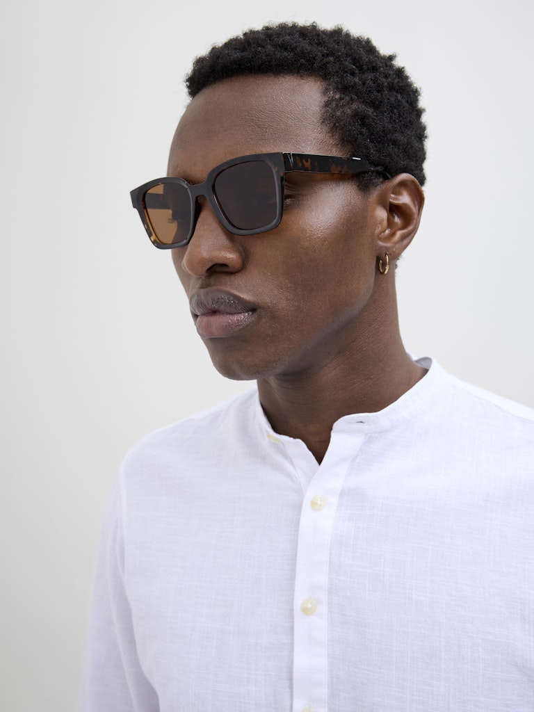 Person wearing dark sunglasses and a white shirt against a plain background