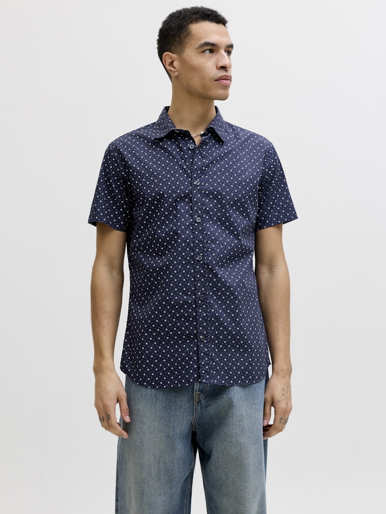Man wearing a navy blue short-sleeve shirt with white polka dots on a light gray background