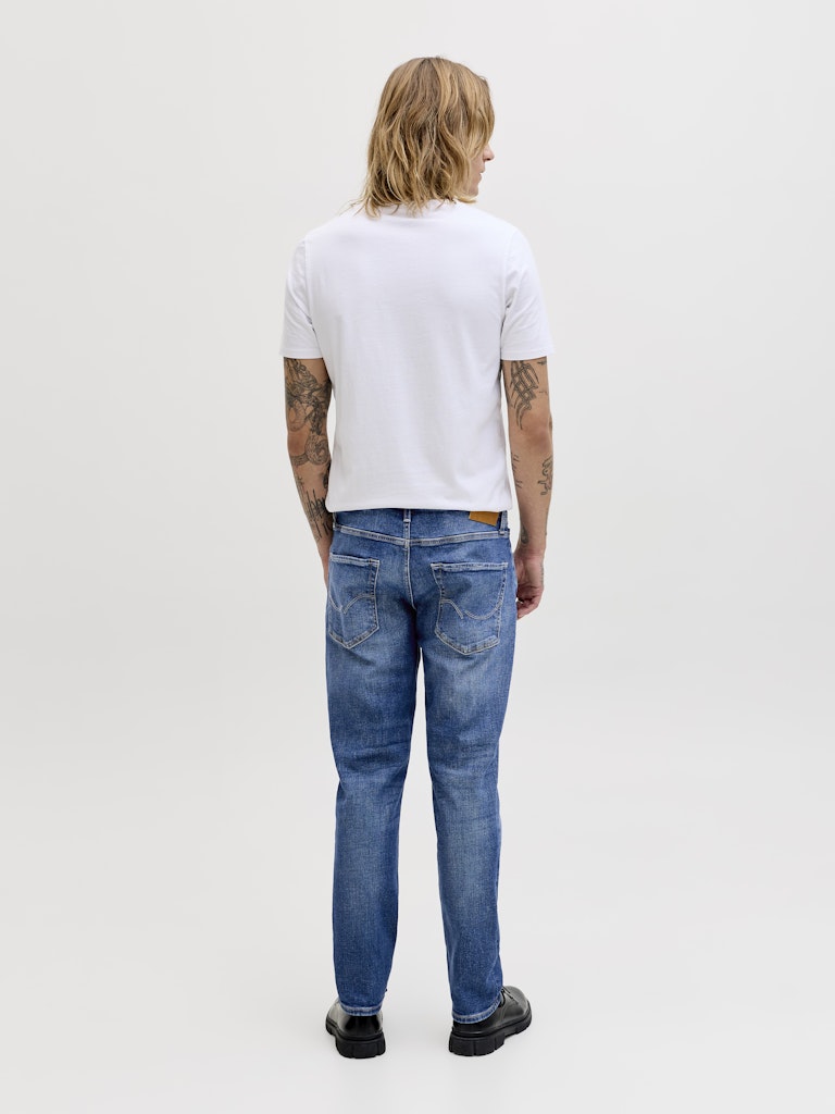 Person wearing a white t-shirt and blue jeans on a plain background