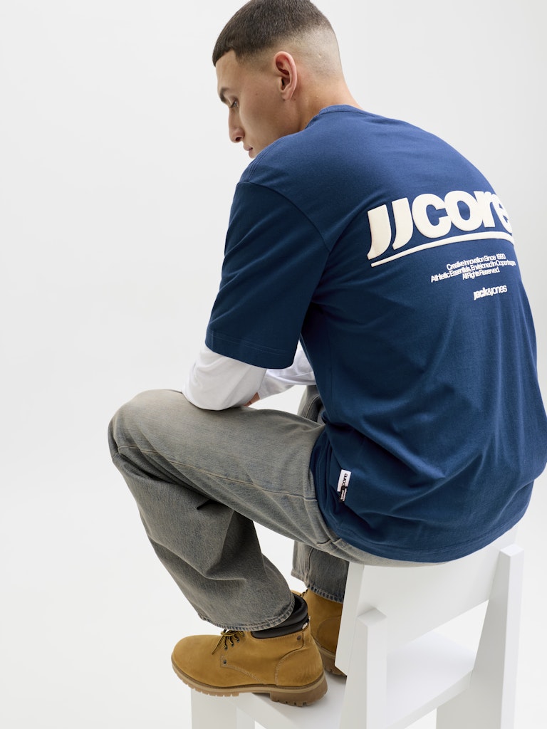 Person wearing a blue sweatshirt with 'JJCORE' branding, sitting on a white stool against a white background.