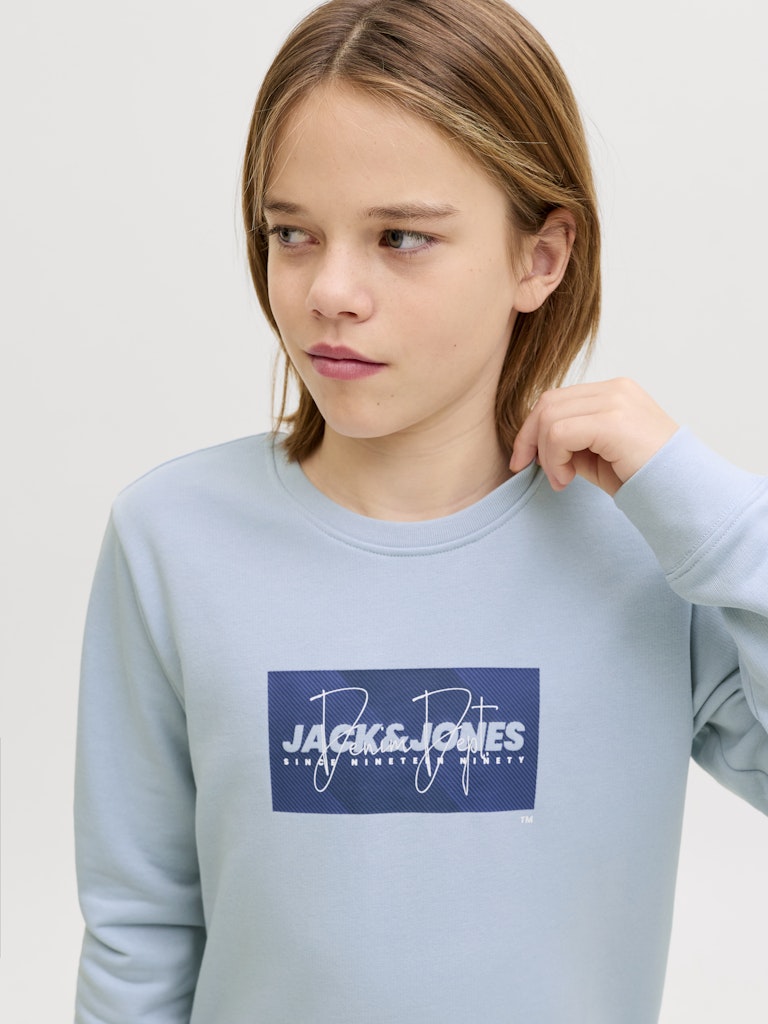 Person wearing a light blue sweatshirt with a Jack & Jones logo on a white background