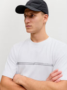 Man wearing a white t-shirt with a logo and a dark cap on a light background