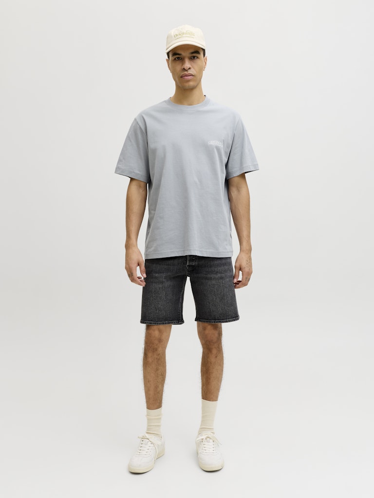 Man wearing a gray t-shirt, black shorts, white socks, and a beige cap on a white background