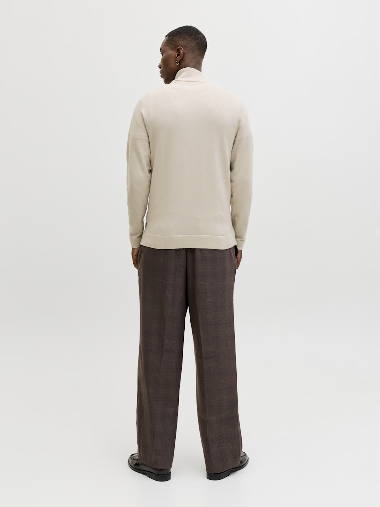 Man wearing a beige sweater and brown pants on a white background