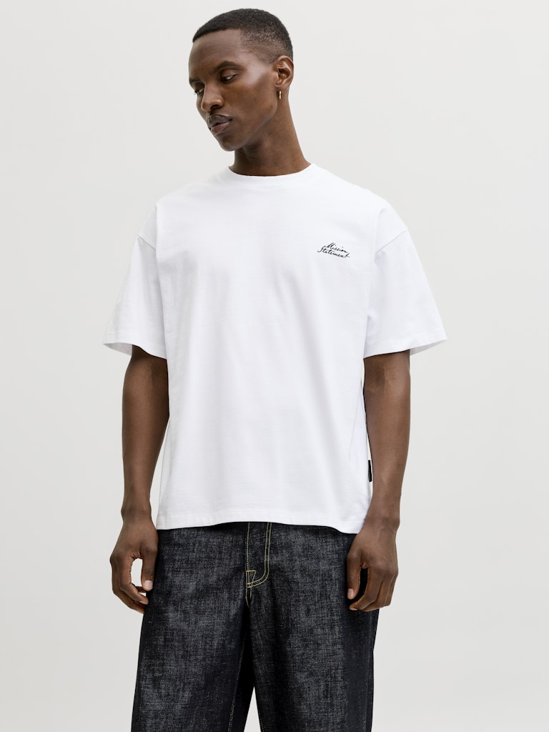 Man wearing a white t-shirt with a small logo on a plain background