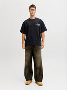 Person wearing a black t-shirt with a logo and dark jeans on a white background