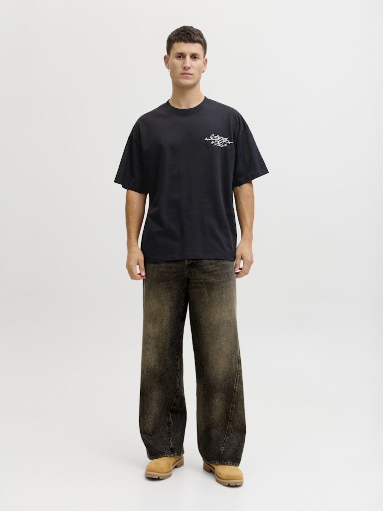 Person wearing a black t-shirt with a logo and dark jeans on a white background