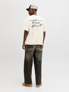 Person wearing a yellow t-shirt with text and dark jeans on a white background