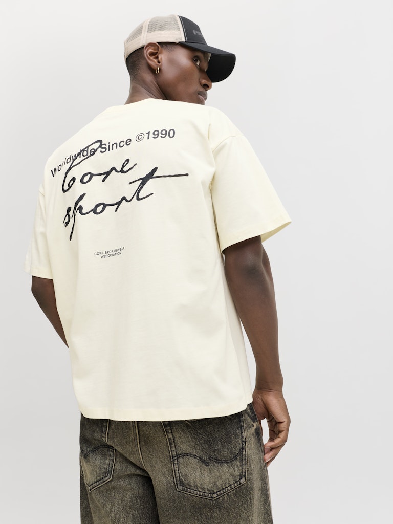 Person wearing a cream t-shirt with text and graphics, standing against a plain background