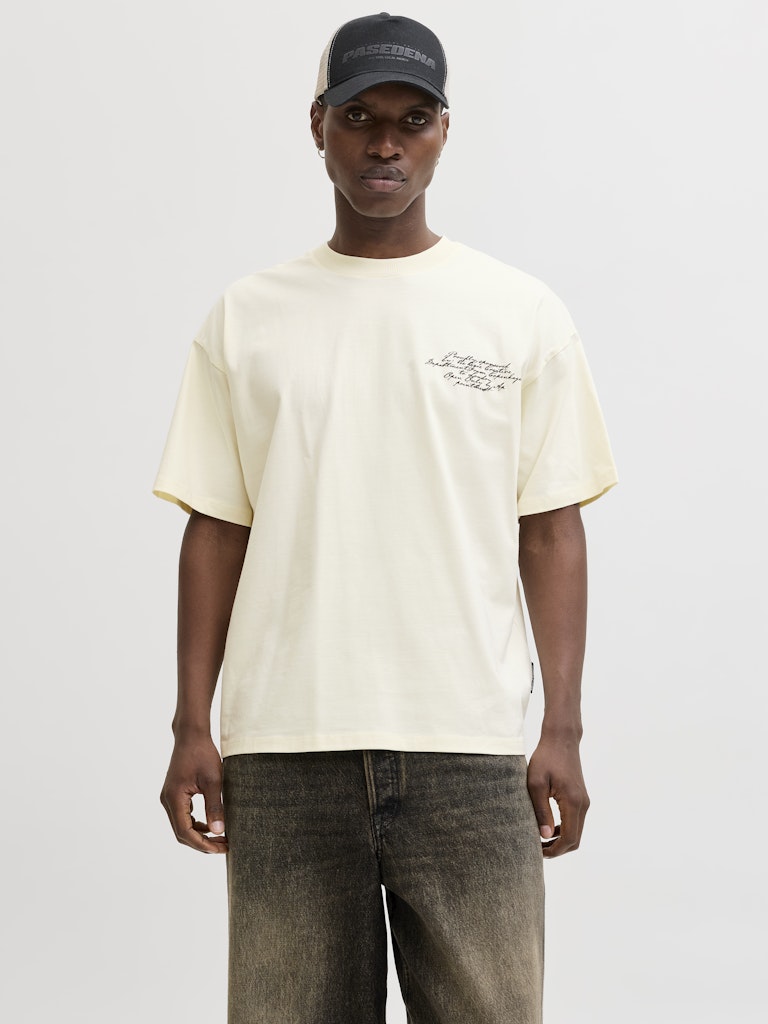 Person wearing a light yellow t-shirt with text and a dark cap on a white background