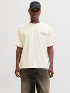 Person wearing a light yellow t-shirt with text and a dark cap on a white background