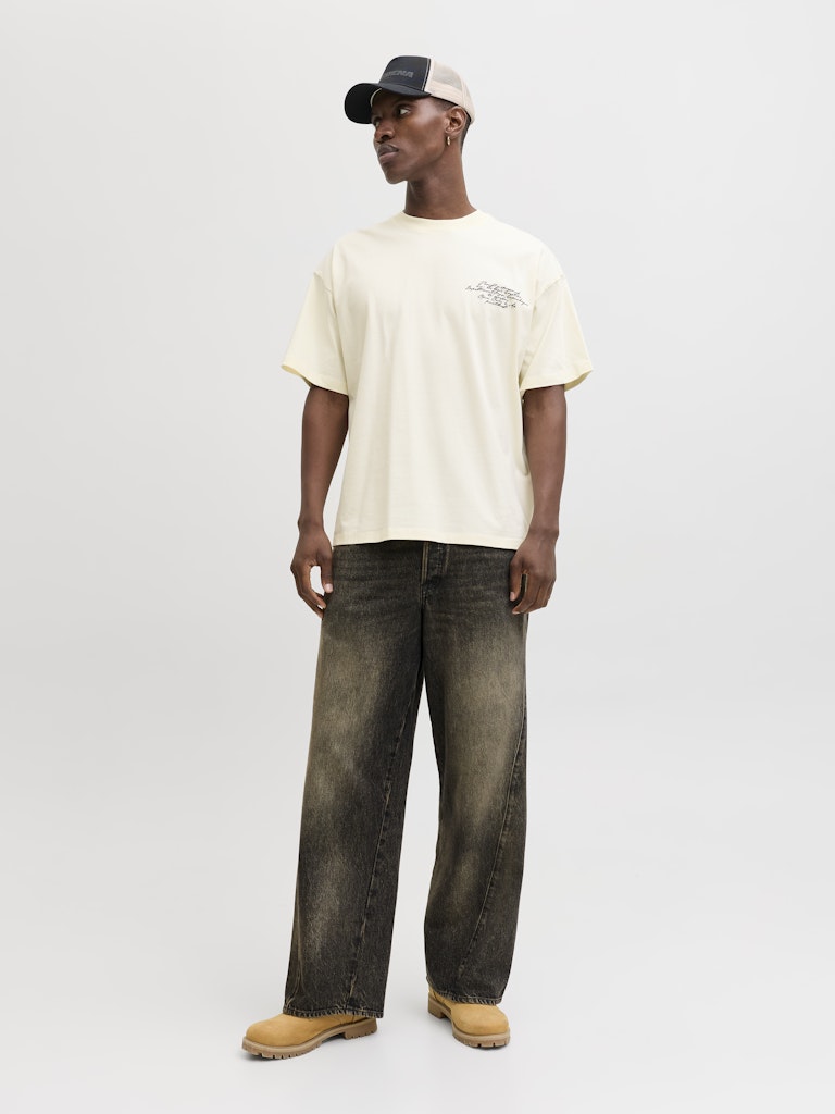 Man wearing a yellow t-shirt, dark jeans, and a cap on a light gray background