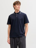 Man wearing a navy polo shirt with white trim on a light gray background