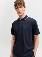 Man wearing a navy polo shirt with white trim on a light gray background
