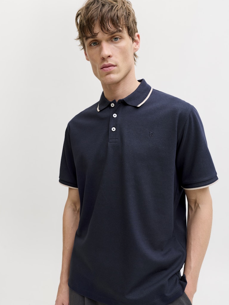 Man wearing a navy polo shirt with white trim on a light gray background