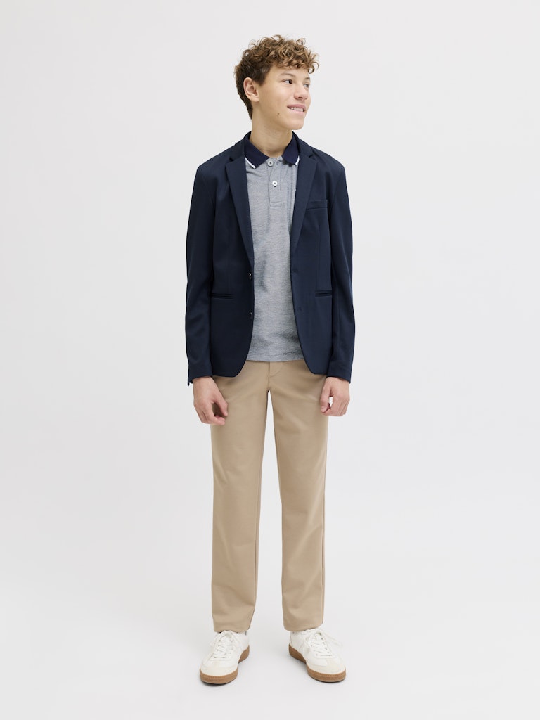 Person wearing a navy blazer, blue polo shirt, beige pants, and white shoes on a light gray background