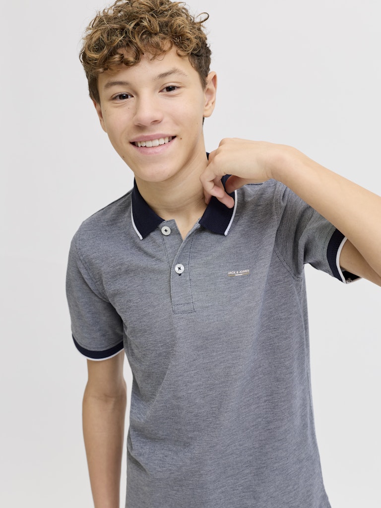 Young boy wearing a blue polo shirt with black trim on a light gray background