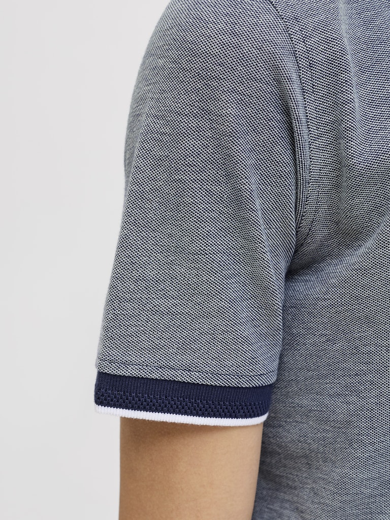 Close-up of a blue polo shirt with navy trim on a light gray background