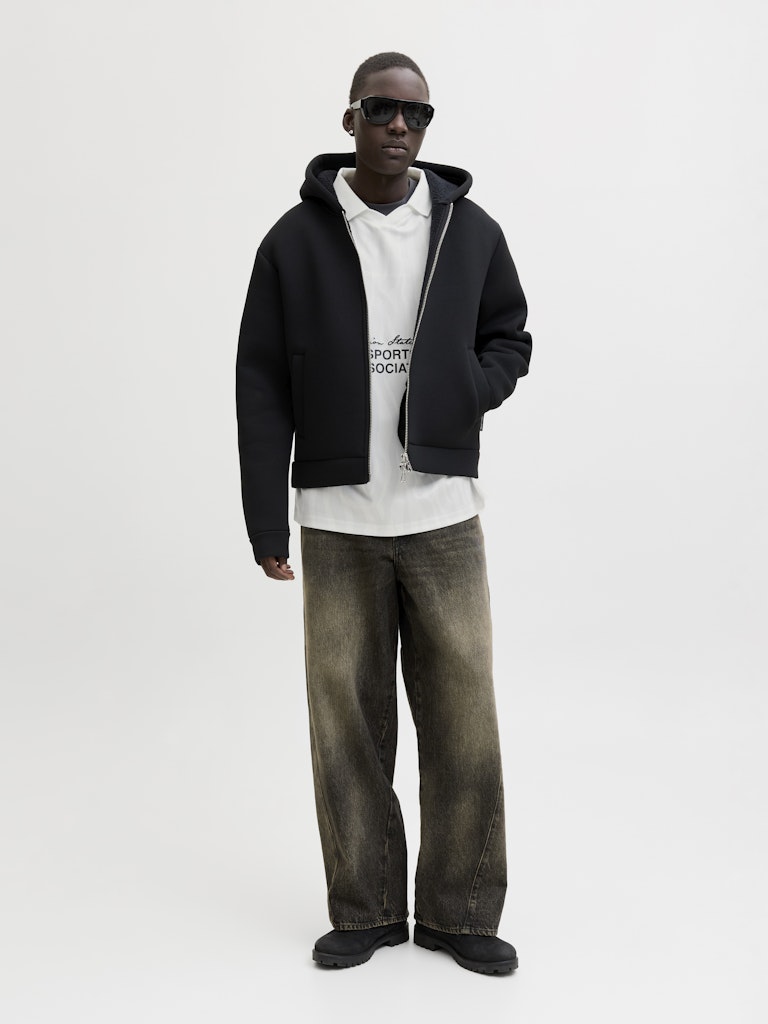 Man wearing a black hoodie, white t-shirt, and dark jeans on a white background