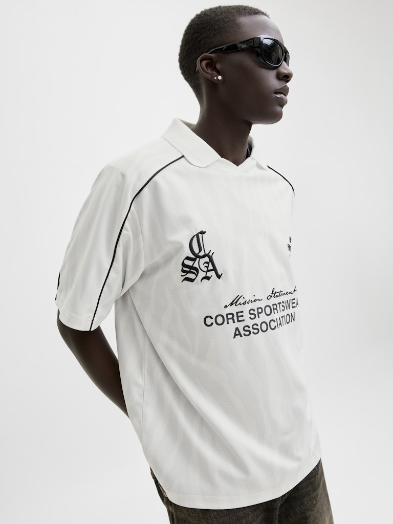 Person wearing a white polo shirt with black text and logos on a plain background