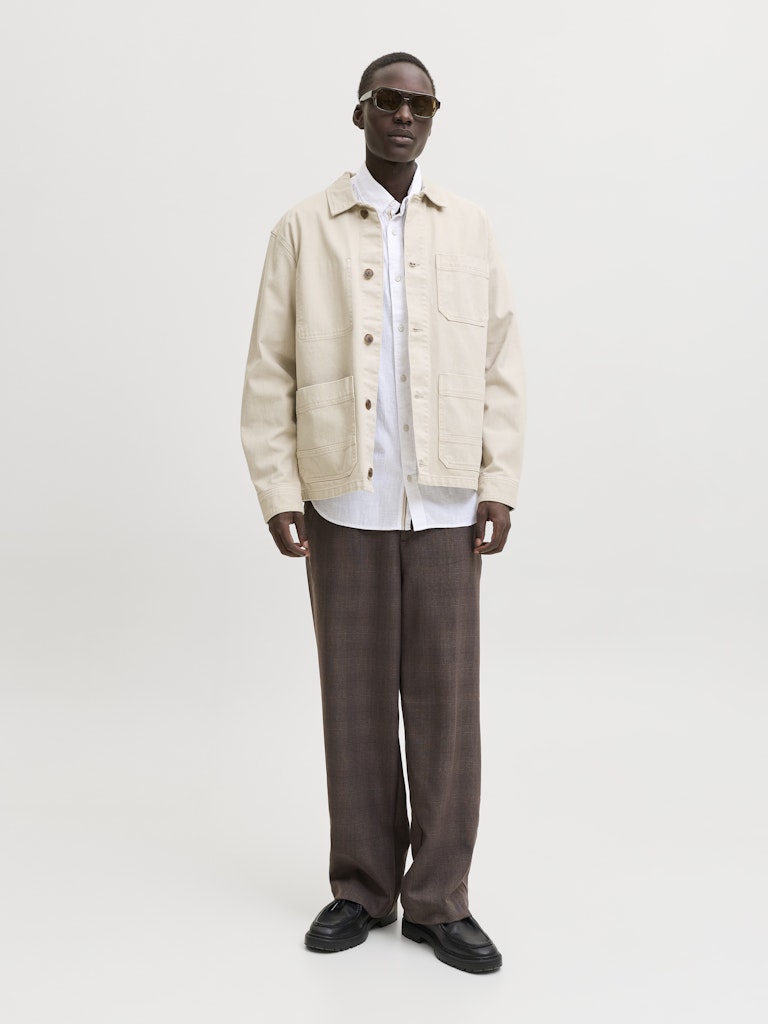 Man wearing a beige jacket, white shirt, and brown pants on a white background