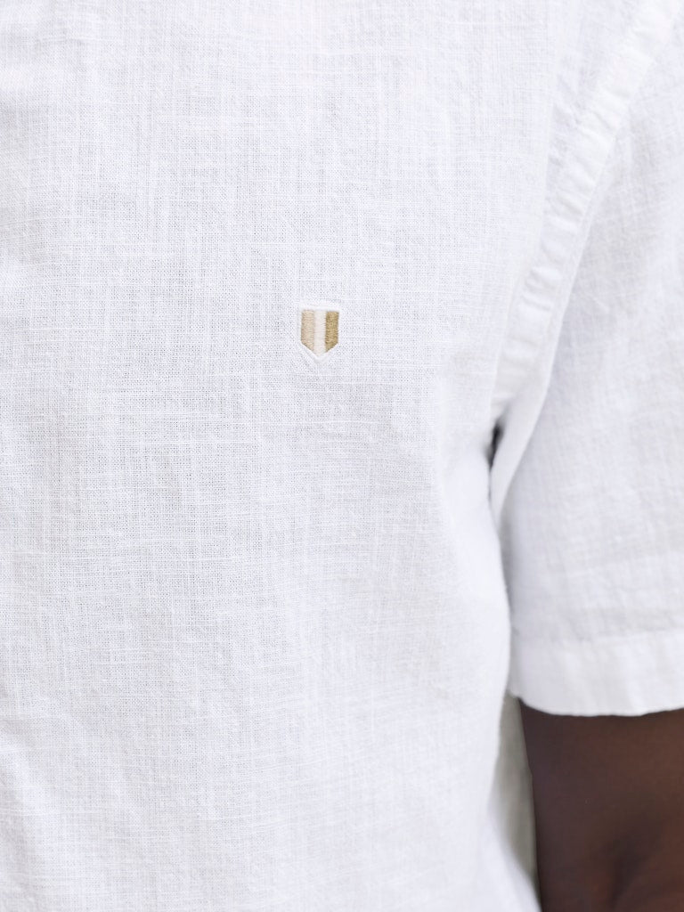 Close-up of a white textured shirt with a small logo on a white background