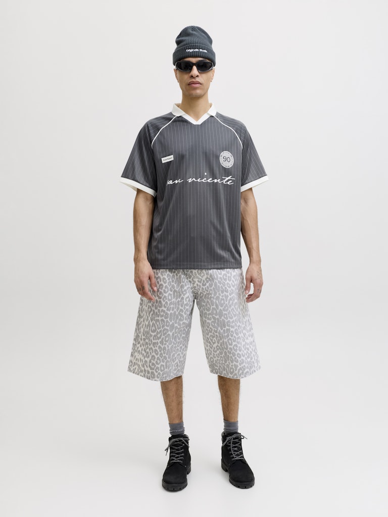 Person wearing a gray sports jersey with patterned shorts, and black shoes on a white background