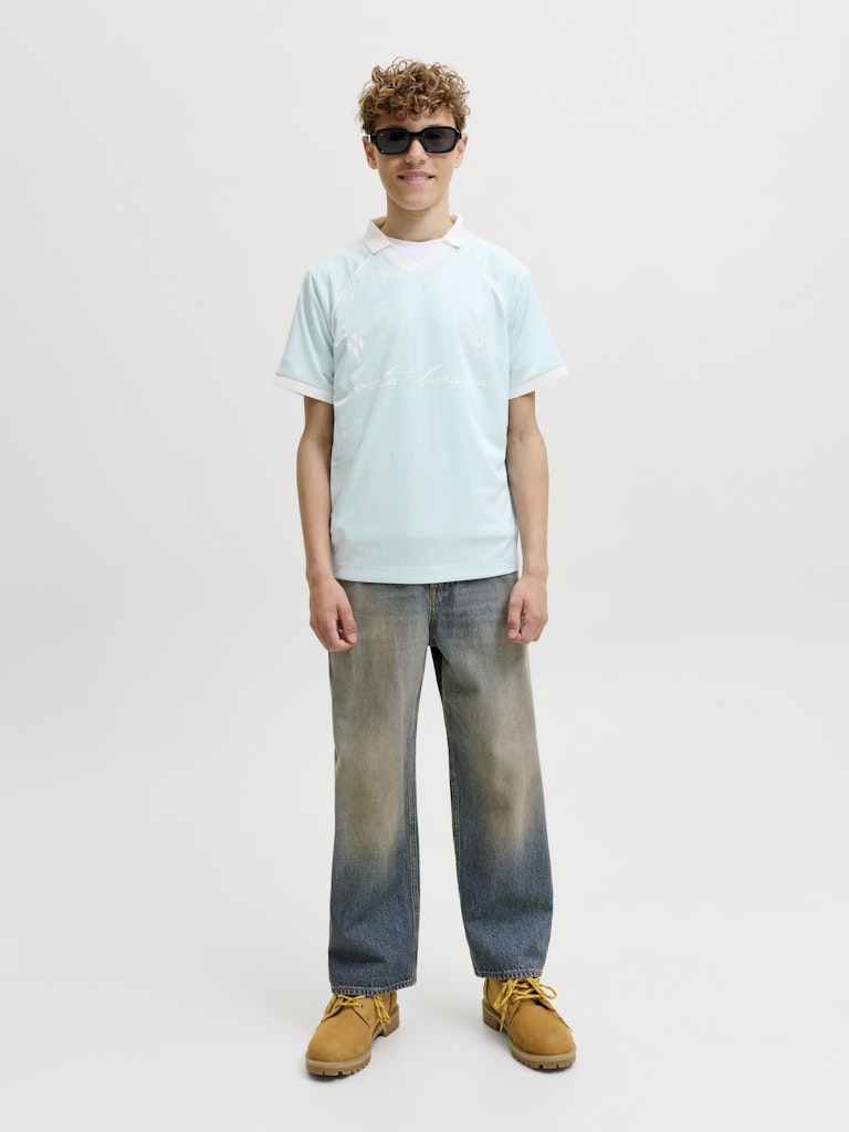 Person wearing a light blue t-shirt, gradient jeans, and brown shoes on a plain background