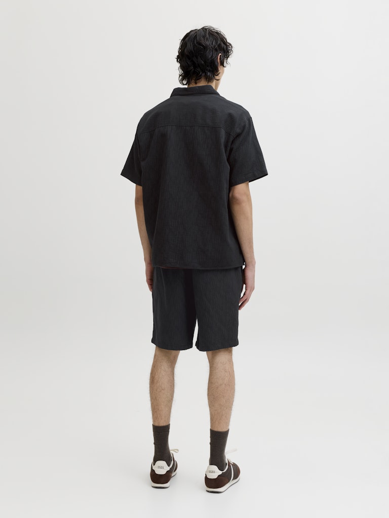 Person wearing a black shirt and shorts set on a white background back view