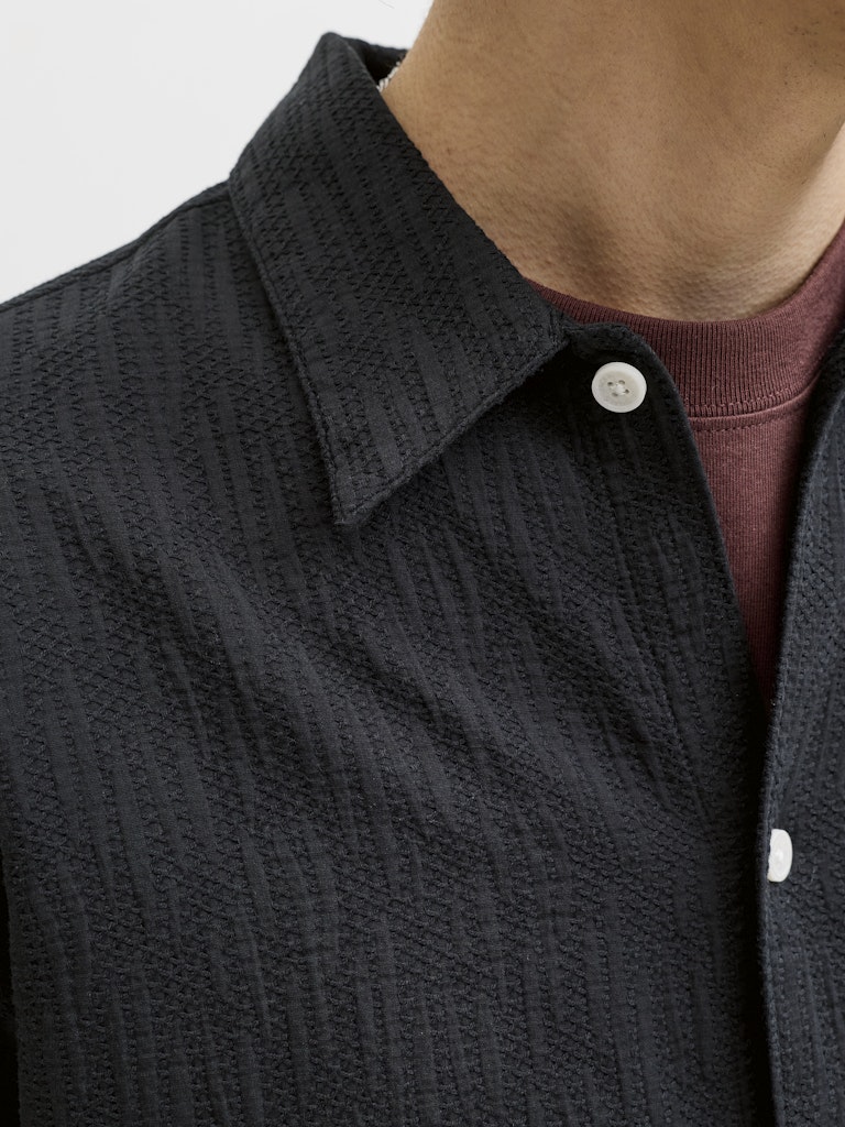 Close-up of a person wearing a textured black shirt with white buttons.