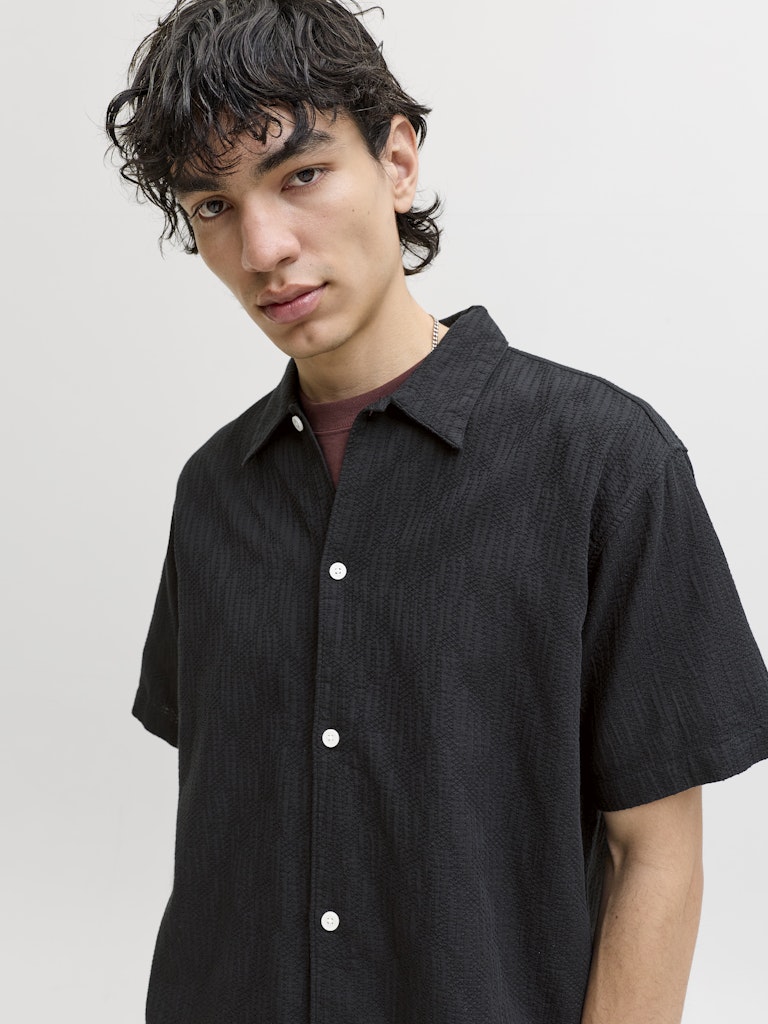 Man wearing a black short-sleeve shirt against a plain background, close up view