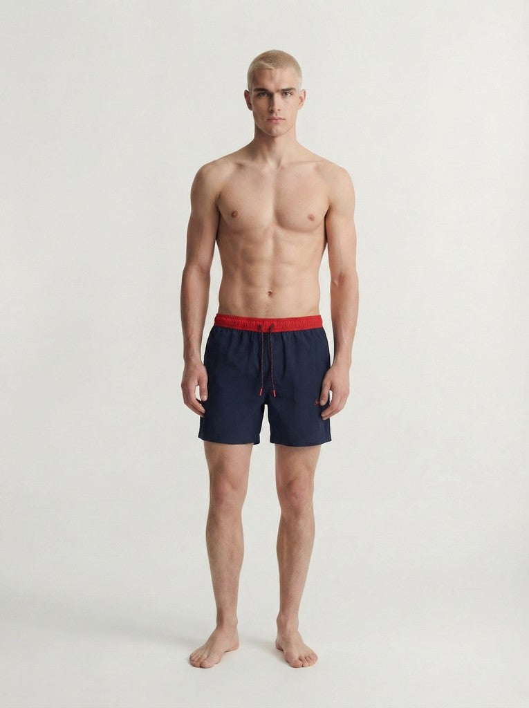 Man wearing navy swim shorts with a red waistband on a white background
