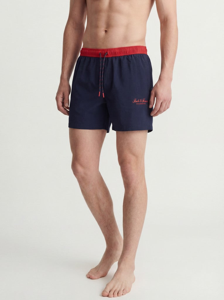 Person wearing navy swim shorts with red waistband on a white background