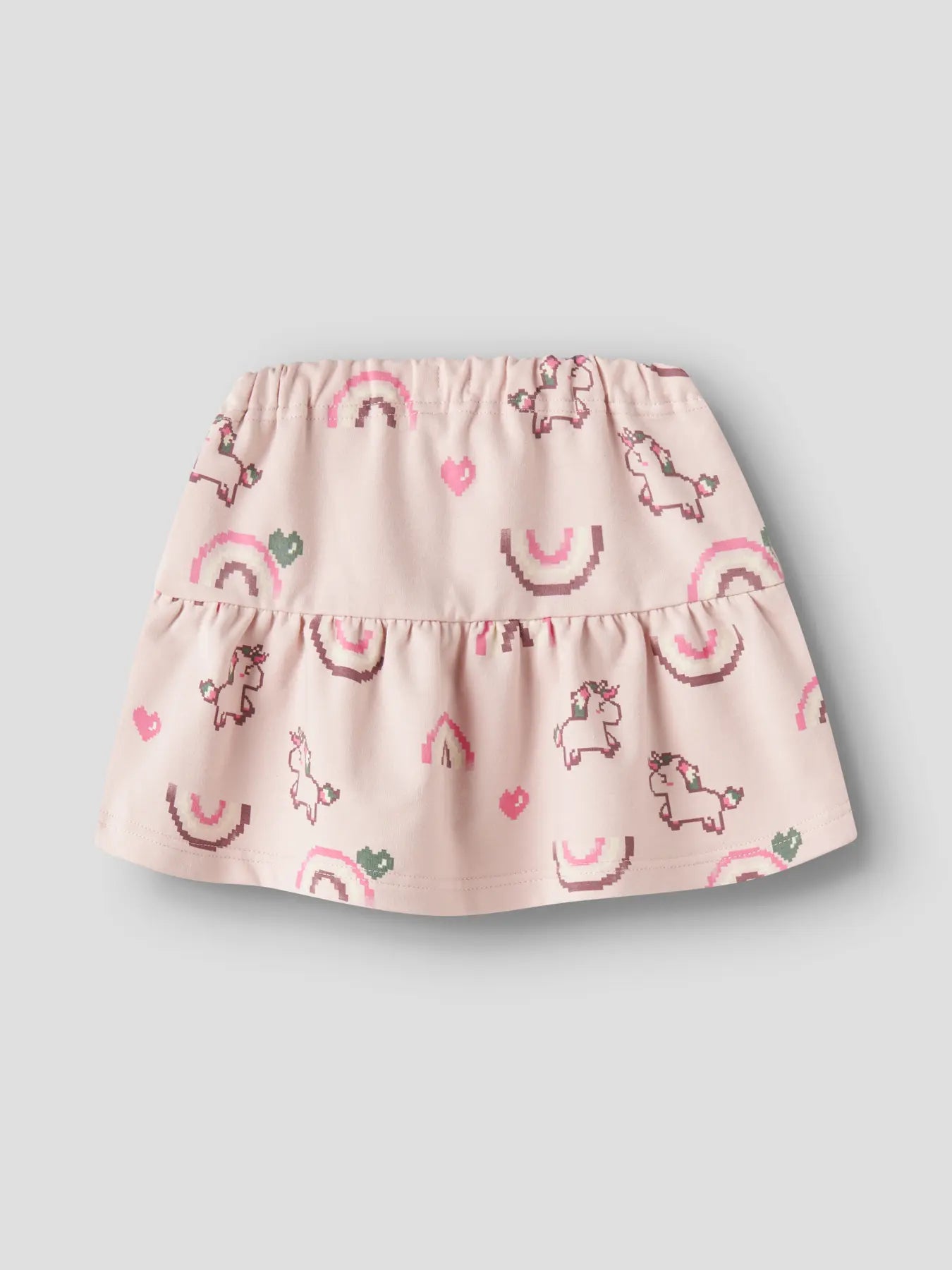 A light pink tiered baby skirt with an all-over print of whimsical unicorns, rainbows, and hearts, shown against a neutral gray background.