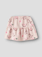 A light pink tiered baby skirt with an all-over print of whimsical unicorns, rainbows, and hearts, shown against a neutral gray background.