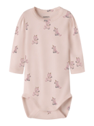 A pale pink long-sleeve baby bodysuit with an all-over print of small pink and lavender unicorns, featuring a crew neck and snap closures at the bottom. The brand name 'nome it' is printed inside the collar.