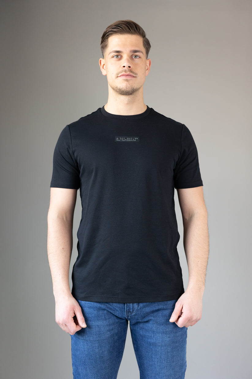 Man wearing a black t-shirt and blue jeans against a gray background