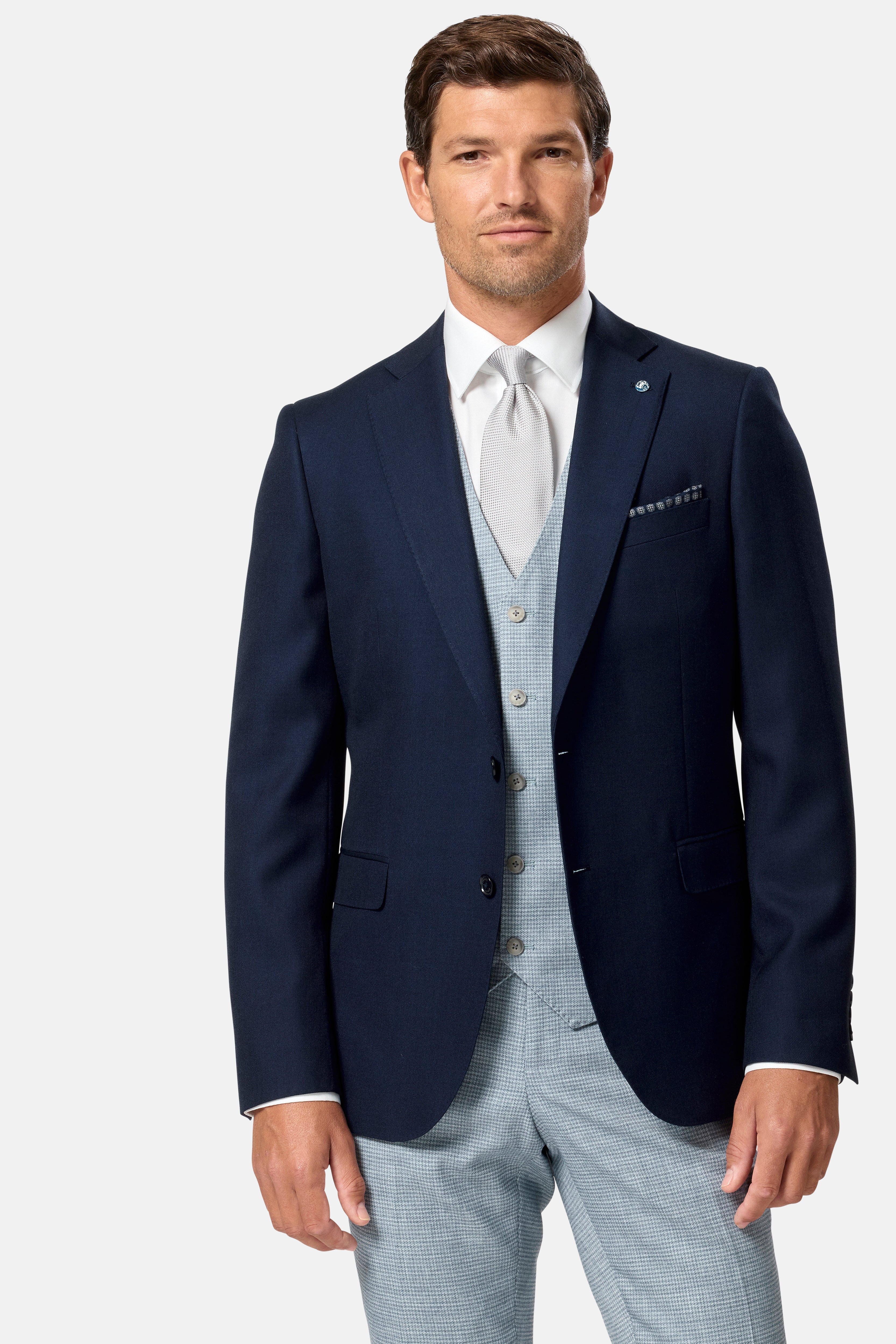 Man wearing a navy blazer, sky waistcoat, white shirt, and light gray pants on a white background