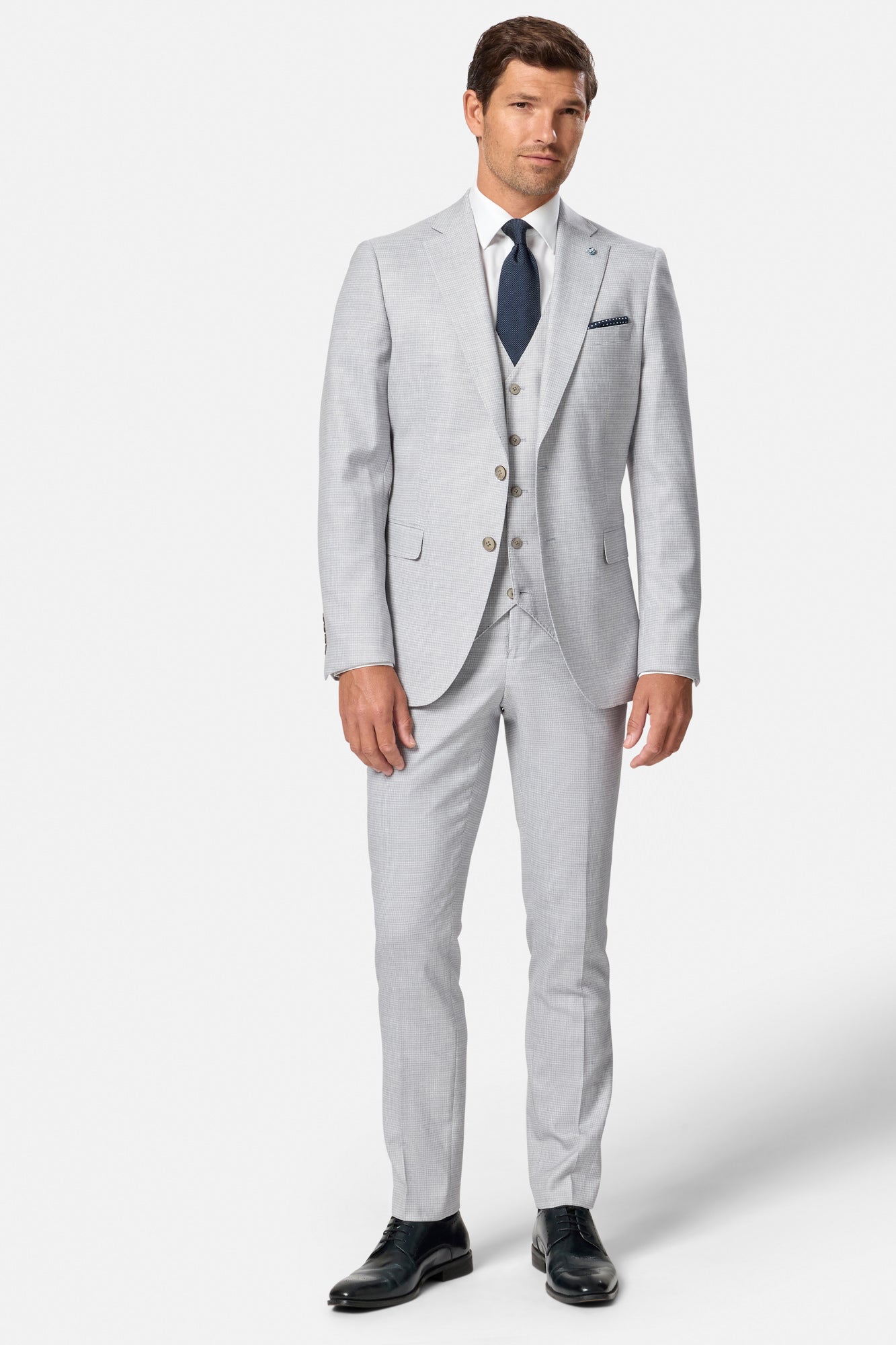 Man wearing a light gray check suit with a white shirt and dark tie on a white background