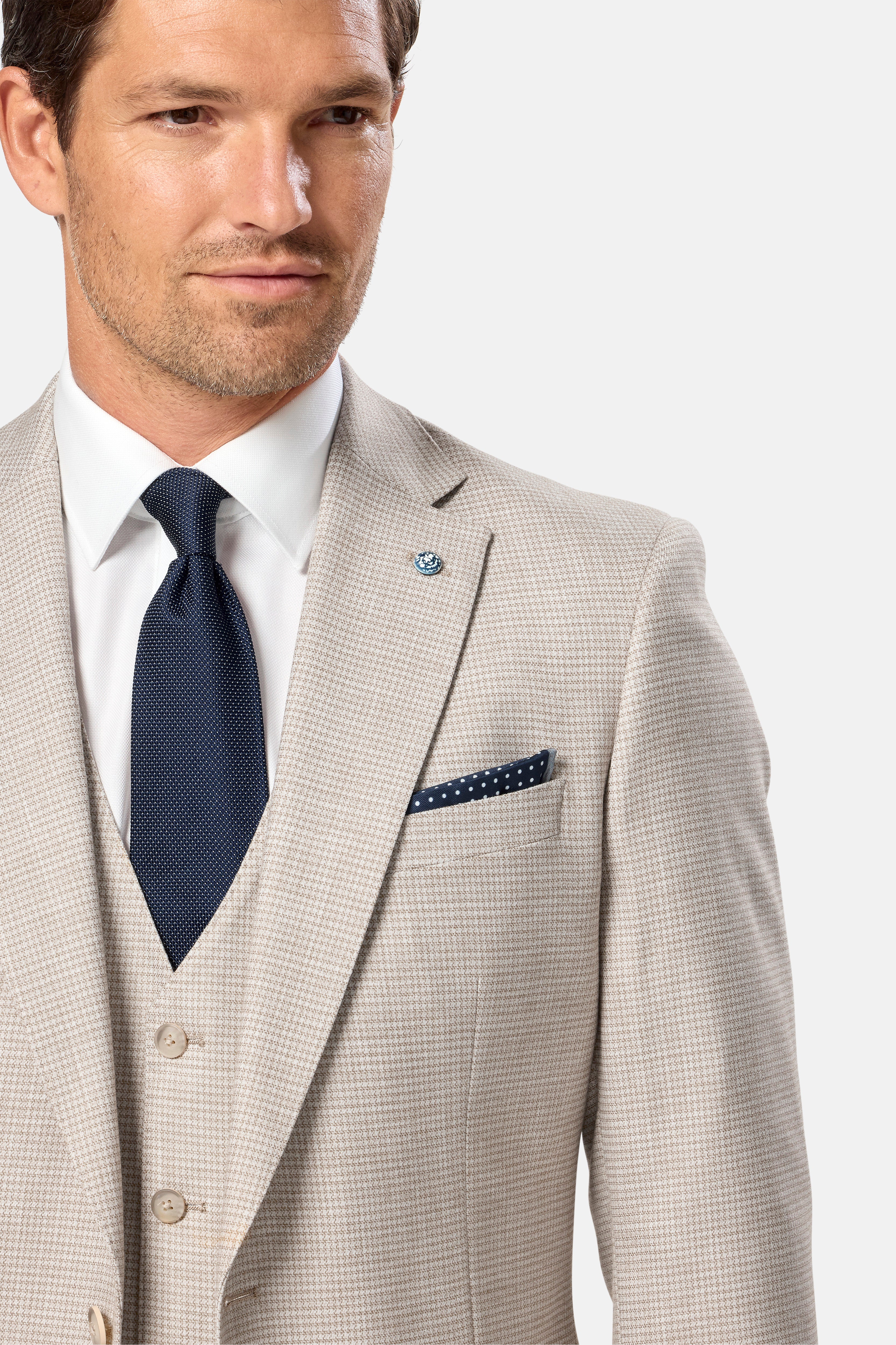 Man wearing a beige suit with a blue tie and pocket square on a light gray background