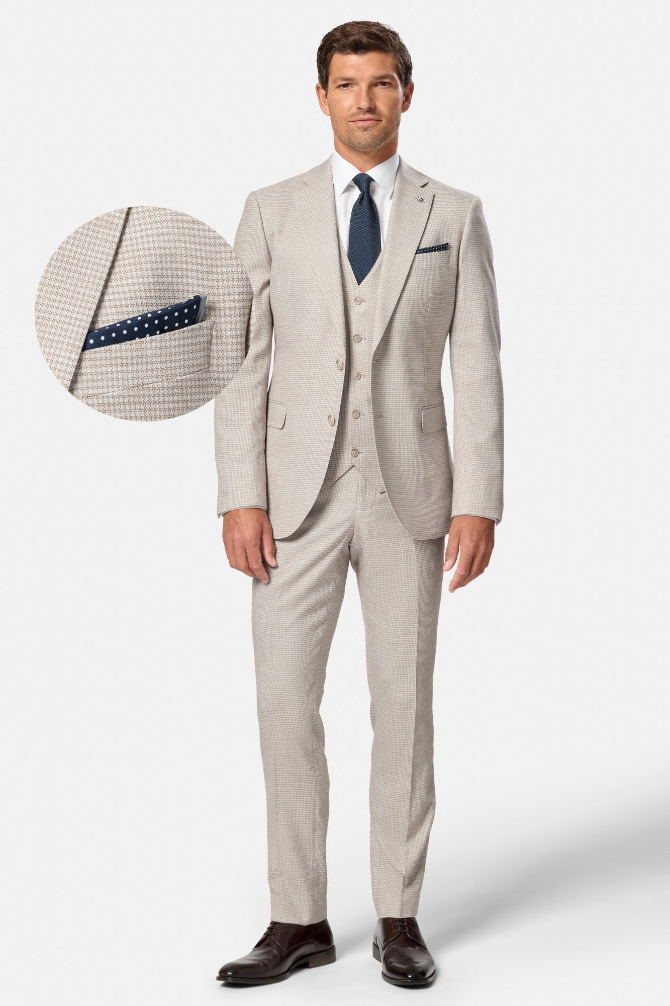 Man wearing a beige Lucas suit with a blue tie and pocket square on a white background