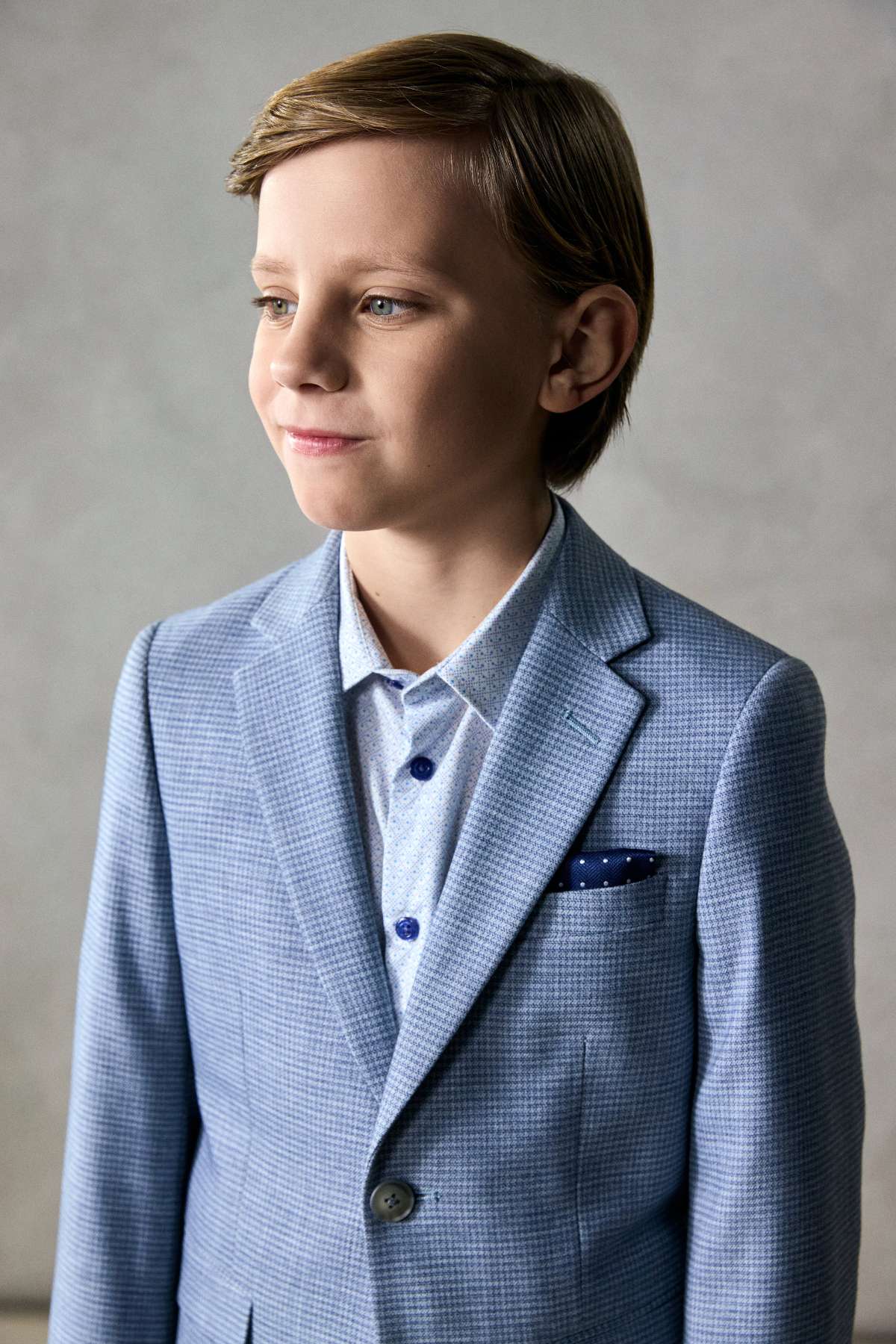 Young boy wearing a light blue checkered suit with a gray background